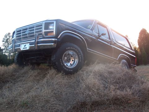 1983 Ford Bronco - This Ford Bronco is angled on a grassy incline, with the sun low in the sky.