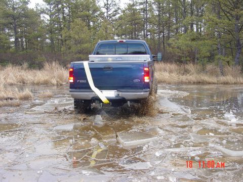 1995 Dodge 1500 - A blue Ford F-250 navigates a frozen, watery terrain, kicking up spray as it drives through the ice.