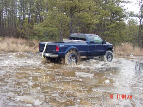 1995 Dodge 1500 - A blue pickup truck navigates through a partially frozen body of water, kicking up spray.