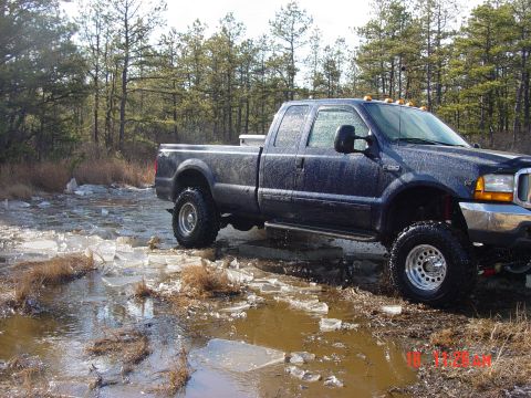 1995 Dodge 1500 - A lifted pickup truck navigates a partially frozen, muddy terrain with trees in the background.