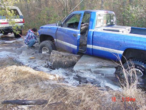 1995 Dodge 1500 - A blue 1995 Dodge 1500 pickup truck is stuck in ice and mud, with a person attempting to free it. Another vehicle is partially visible in t…
