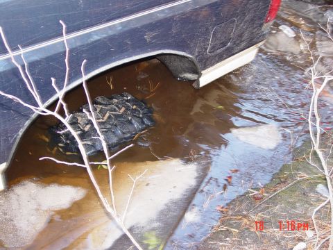 1995 Dodge 1500 - A dark blue pickup truck's rear wheel well is partially submerged in murky water, with a tire visible below the surface.