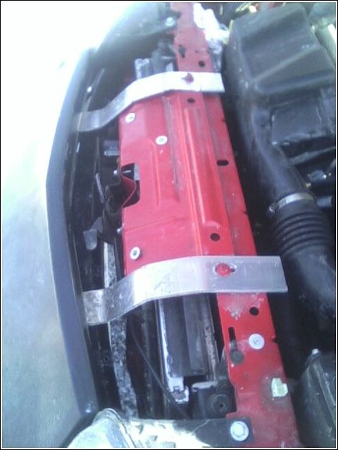 2005 Chevrolet Cavalier - Close-up view of the engine bay radiator support structure, showing red painted metal and silver mounting brackets.