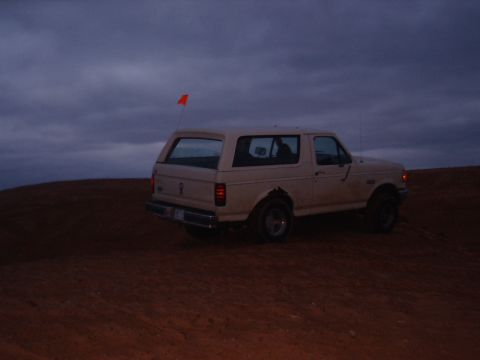 1991 Ford Bronco - A tan 1991 Ford Bronco is parked on a sand dune with an orange flag flying.
