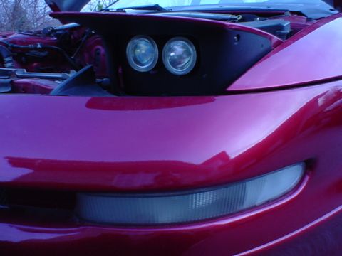 1993 Ford Probe - The front corner of a red sports car is shown with its hood open, revealing the headlight assembly.