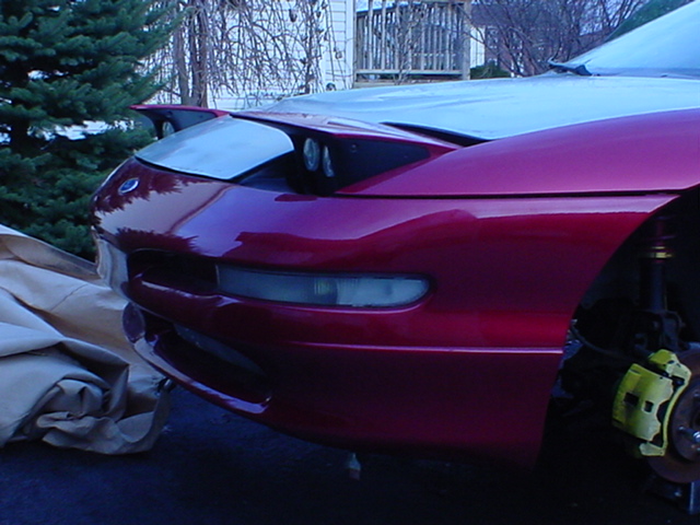 Red 1993 Ford Probe front end with pop-up headlights, one partially open. Yellow brake caliper visible
