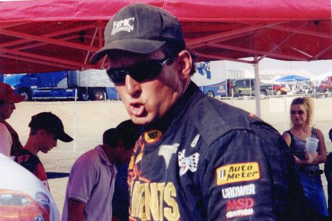 1995 Ford Bronco - A man in racing attire stands in front of tents and vehicles at an outdoor event.