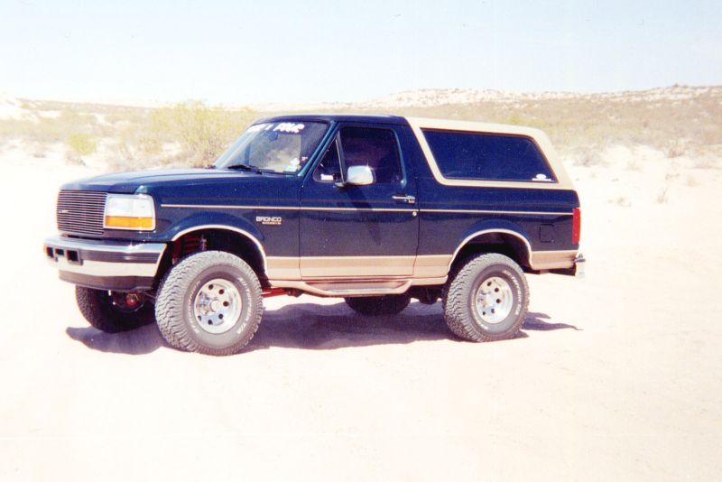 Dark blue and tan Ford Bronco parked on sand, front 3/4 view
