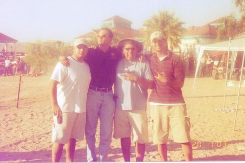 1995 Ford Bronco - Group of four men posing for a photo on a beach with tents and buildings in the background.