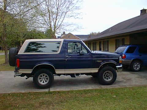 1992 Ford Bronco - A side view of a 1992 Ford Bronco parked in a driveway with another vehicle in the background.