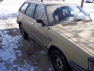 1972 Ford Ranchero - The side of a tan Subaru station wagon is visible, parked on a concrete driveway with patches of snow.