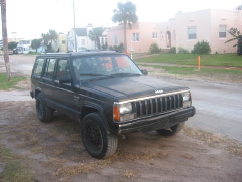 1989 Ford Bronco - This black Jeep Cherokee XJ is parked on a dirt road with houses in the background.