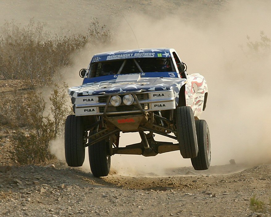 1998 Chevrolet C/K Pickup truck mid-air, decorated with stars and stripes, kicking up dust