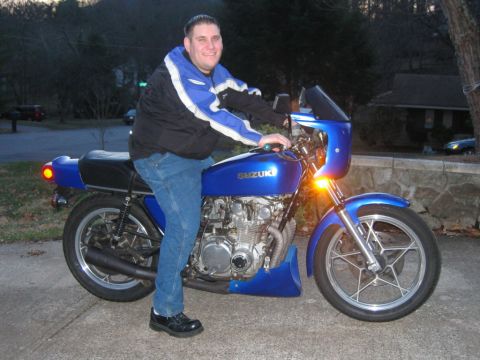 1985 Ford LTD Crown Victoria - Man on a blue Suzuki motorcycle parked on a paved surface outdoors.