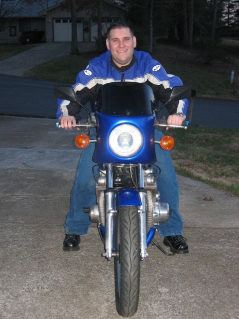 1985 Ford LTD Crown Victoria - A man sits on a blue motorcycle parked on a driveway in front of a house.
