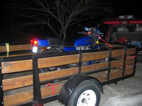 1985 Ford LTD Crown Victoria - Motorcycle being transported in a trailer at night.