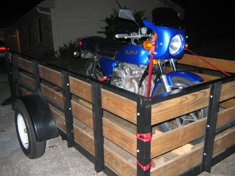 1985 Ford LTD Crown Victoria - A blue Suzuki motorcycle is being transported in a wooden trailer at night.