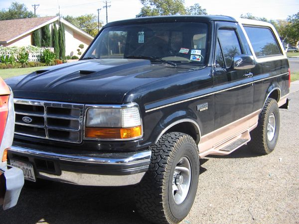 Black Ford Bronco SUV with tan lower trim, hood scoops and all-terrain tires, parked in a driveway