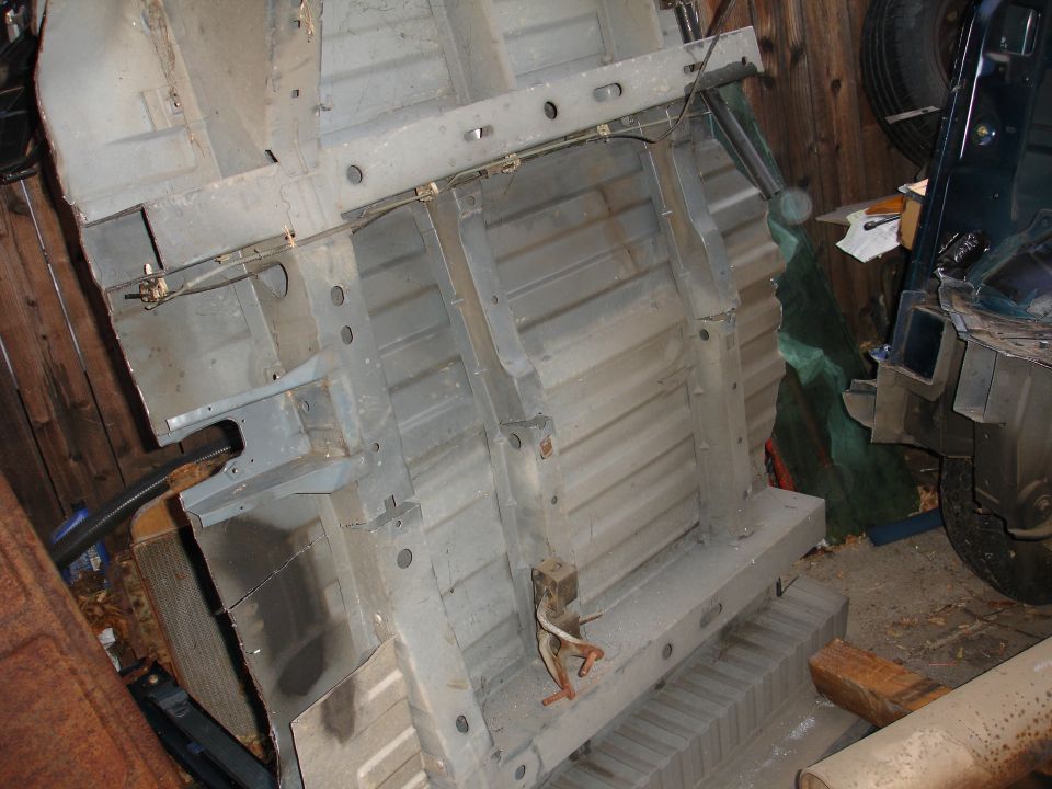 Underside of a vehicle chassis, showing frame rails and floor pan. Another vehicle is partially visible to the right