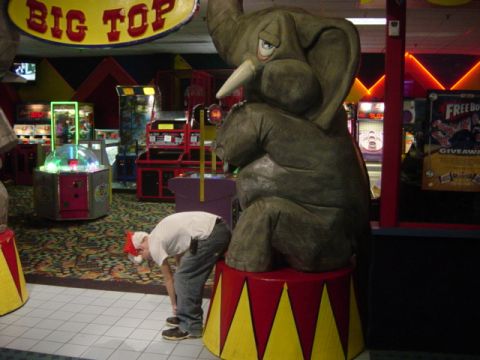 1995 Ford Probe - A person in a Santa hat bends over near a large elephant statue in an amusement arcade filled with games.