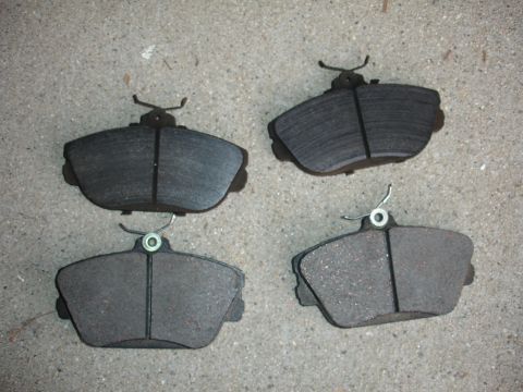 1995 Ford Taurus - Four brake pads are laid out on a concrete surface, showing wear and hardware.