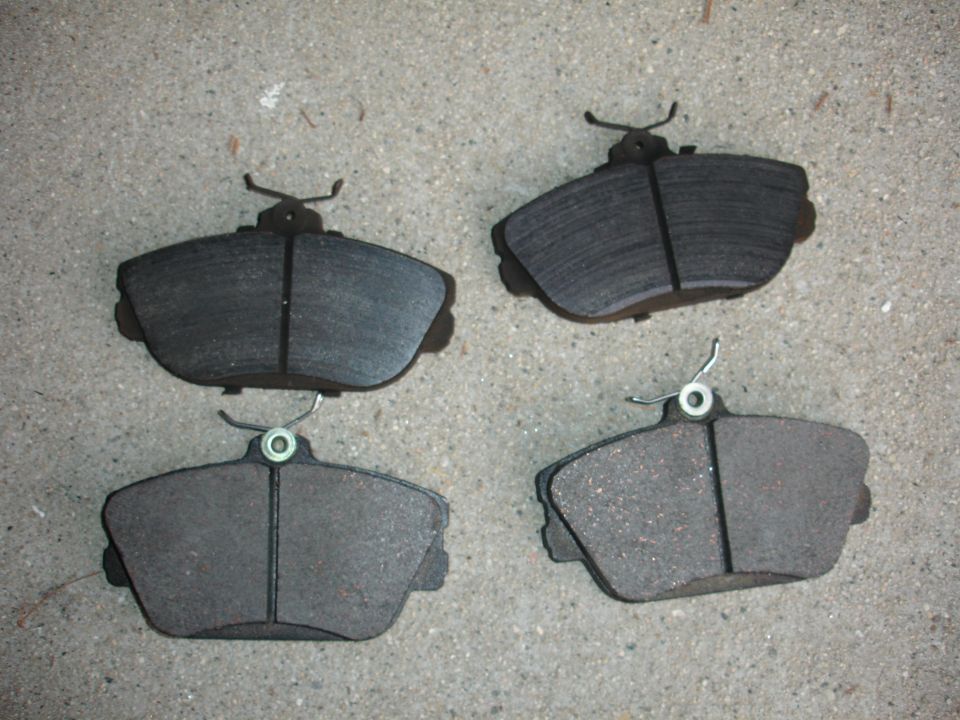 Four brake pads with metal shims and clips on a concrete surface