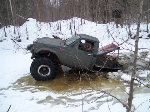 1995 Ford Bronco - A heavily modified pickup truck is stuck in a frozen body of water surrounded by a snowy forest.