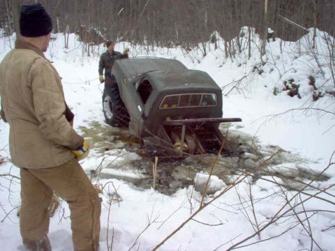 1995 Ford Bronco - Two people attempt to free an off-road vehicle stuck in icy water during winter.
