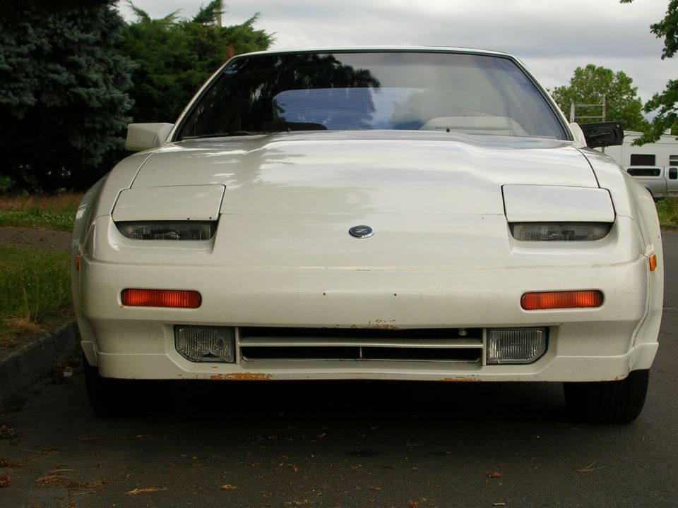 Front view of white Nissan 300ZX Z31 with pop-up headlights partly open and Z nose badge