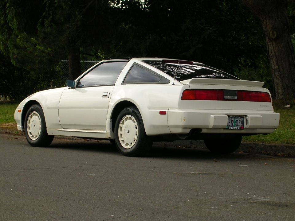 White Nissan 300ZX coupe rear three-quarter view at curb with spoiler and white alloy wheels