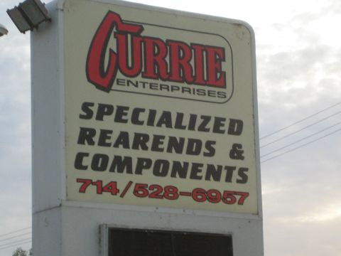 1990 Ford Bronco - roadside pole sign for Currie Enterprises advertising specialized rearends and components against an overcast sky.