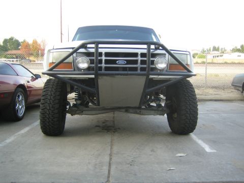 1990 Ford Bronco - Front view of a lifted Ford pickup fitted with a tubular front bumper, round auxiliary lights, and large off-road tires in a parking lot.