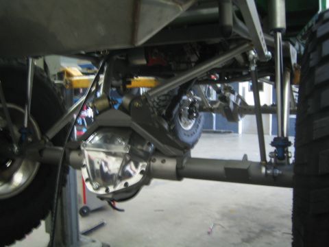 1990 Ford Bronco - Underside view of a lifted vehicle on a shop hoist, showing the rear axle, differential cover, and suspension links.