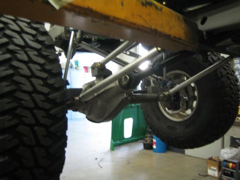 1990 Ford Bronco - Underside view of a raised vehicle showing the axle, four-link suspension, and large off-road tires in a shop.