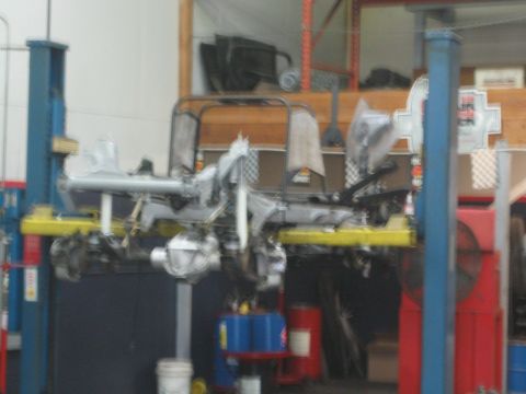 1990 Ford Bronco - blurry image of a stripped vehicle chassis raised on two-post lifts inside a busy automotive shop.