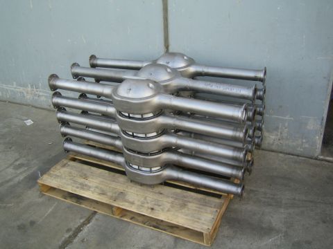 1990 Ford Bronco - stack of unpainted fabricated axle housings resting on a wooden pallet against a concrete wall.