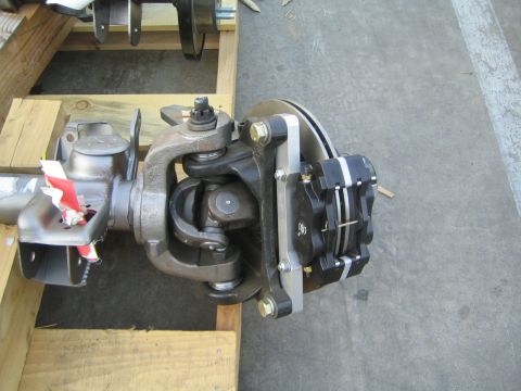 1990 Ford Bronco - Close-up of an assembled axle end showing the steering knuckle, disc brake rotor, and caliper resting in a wooden crate.