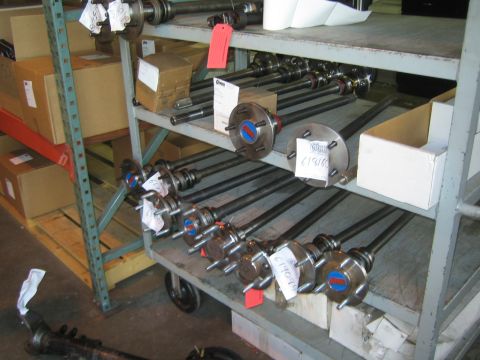 1990 Ford Bronco - Rows of tagged axle shafts with flanges laid out on a metal warehouse shelving cart alongside parts boxes.