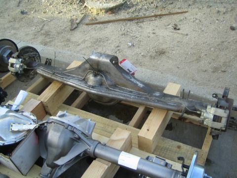 1990 Ford Bronco - fabricated welded axle housing with a brake assembly resting on wooden crates in a sandy outdoor lot.