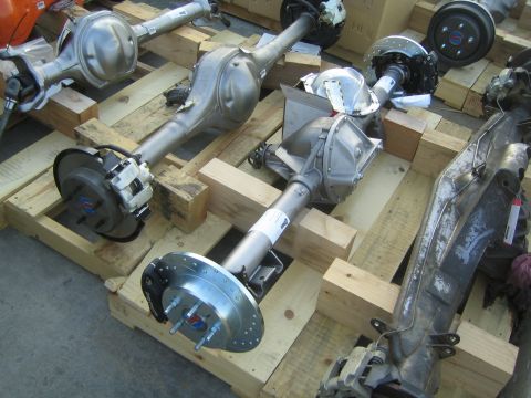 1990 Ford Bronco - assembled vehicle axle with drilled disc brake rotors and a differential center section staged on wooden crates.