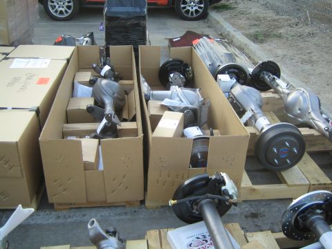 1990 Ford Bronco - Differential center sections packed in cardboard boxes next to assembled axles on a pallet in an outdoor lot.