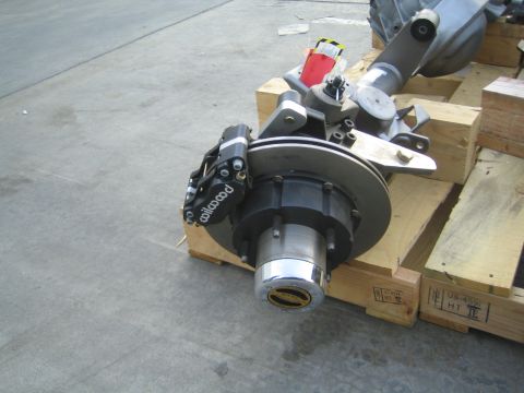 1990 Ford Bronco - Close-up of an axle end fitted with a black Wilwood brake caliper and rotor, resting on a wooden crate on the shop floor.