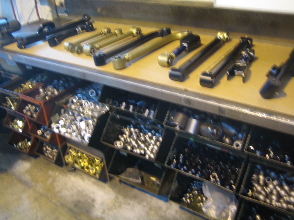 Suspension control arms on a workbench above bins of bushings and hardware