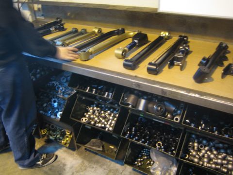 1990 Ford Bronco - person standing at a workbench covered with fabricated suspension arms above bins of bushings and assorted parts.
