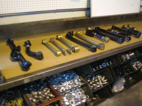 1990 Ford Bronco - assortment of fabricated suspension control arms and links arranged on a workbench above bins of hardware.