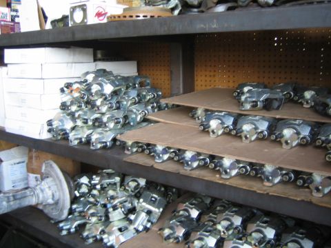 1990 Ford Bronco - Warehouse shelves stacked with rows of zinc-plated remanufactured brake calipers and parts boxes.