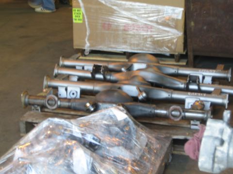 1990 Ford Bronco - row of bare steel axle housing tubes and center sections rests on pallets near a crated part on a shop floor.