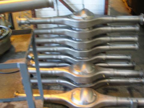 1990 Ford Bronco - neat stack of machined bare-metal axle housing tubes rests on a steel support rack in a shop.
