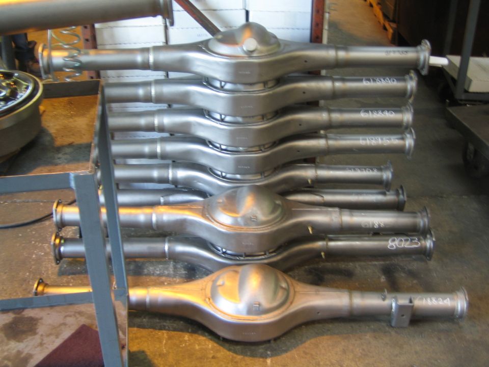 Stacked machined axle housings with handwritten numbers on a rack