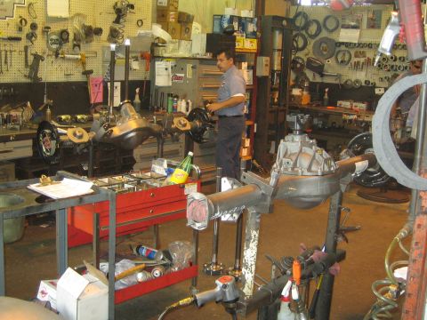 1990 Ford Bronco - technician works among differential and axle assemblies in a cluttered shop with tool walls and bins.